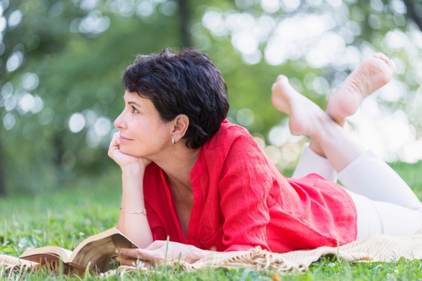 Mature woman lying on grass and reading book.