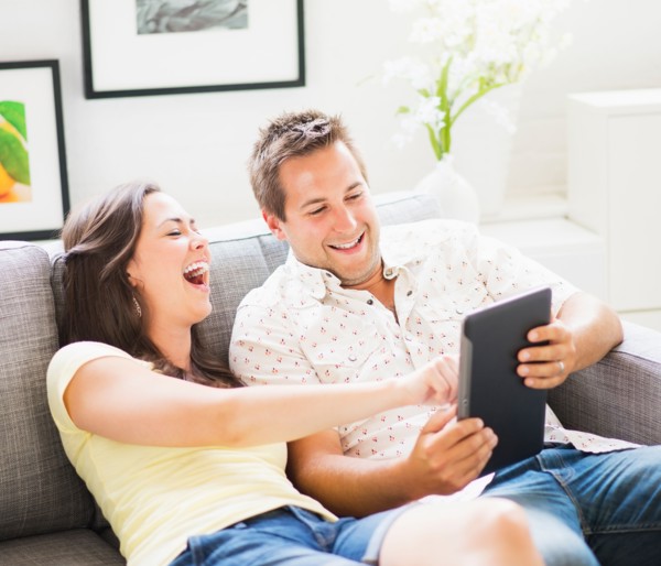 Portrait of playful couple using digital tablet on sofa