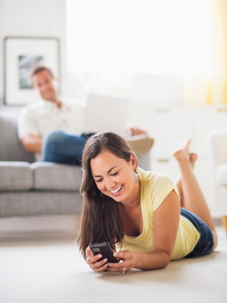 Woman lying on front and using mobile phone, man in background