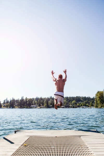 Young man jumping to lake from jetty