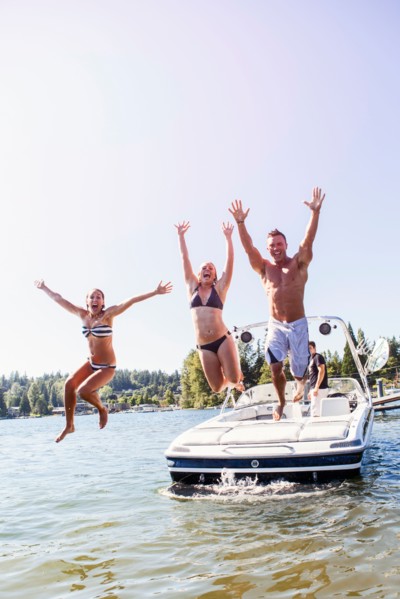 Young people jumping to lake from motorboat