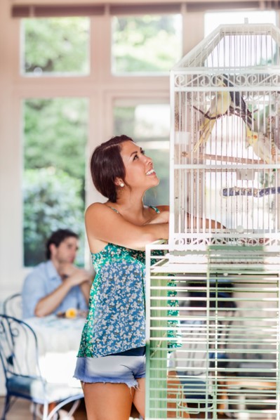 Woman standing by bird cage, man in background