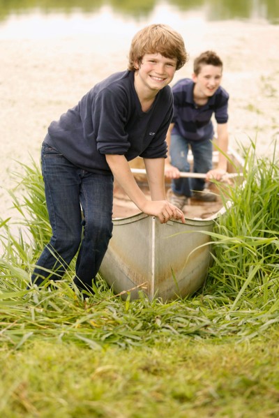 Two boys (12-13) posing with boat on grass near lake