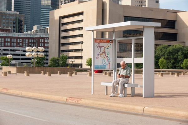 Senior man sitting at bus stop and text messaging