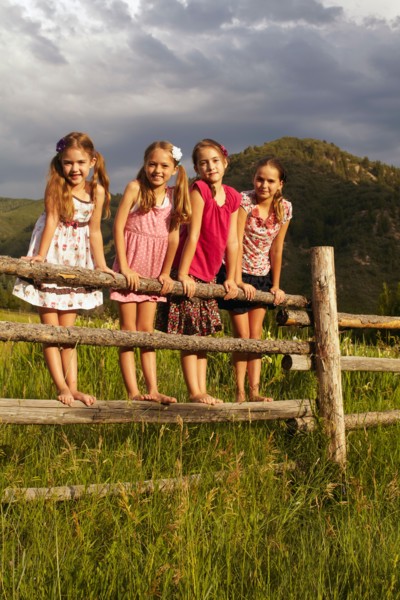Four girlfriends (6-7, 8-9, 10-11) standing on wooden fence in grass