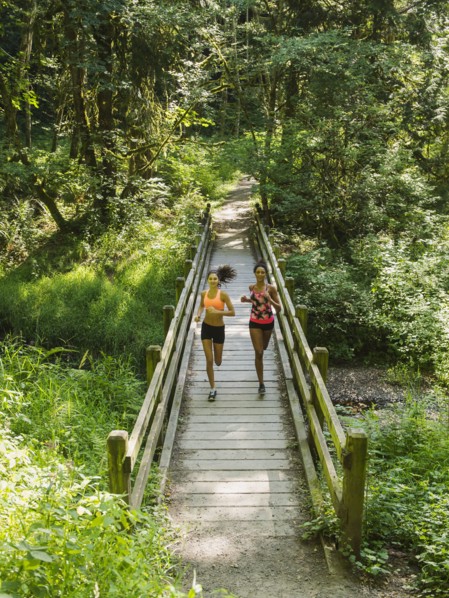 Two young women running over wooden footbridge. USA, Oregon, Portland.