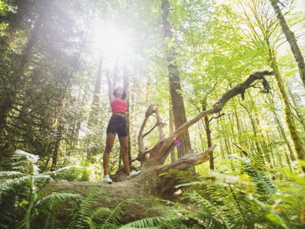 Young woman standing on log in forest. USA, Oregon, Portland.