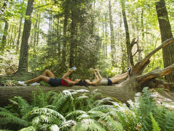 Young women reading book on log in forest. USA, Oregon, Portland.