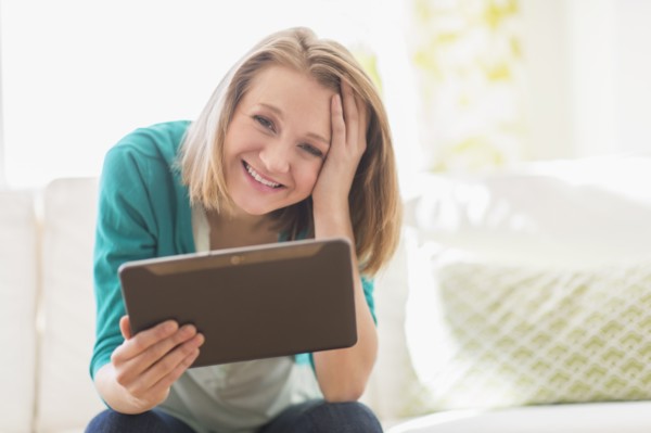 Portrait of woman on sofa holding digital tablet.