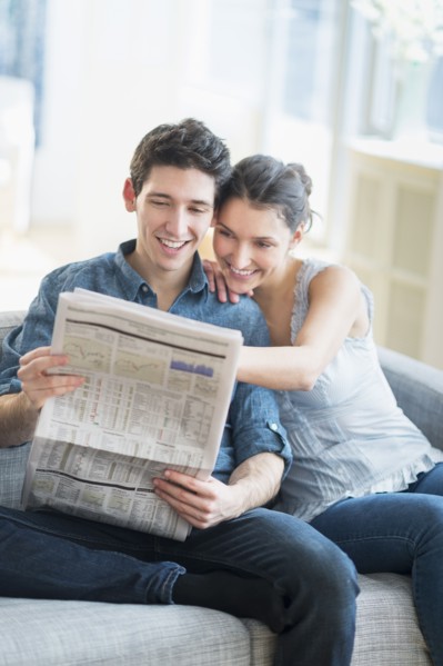 Couple reading newspaper on sofa.