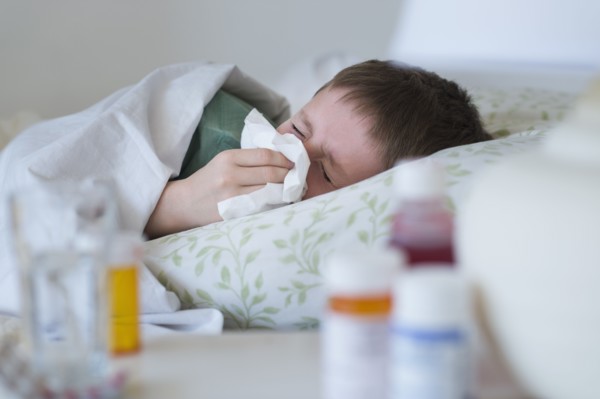 boy (8-9) lying in bed and blowing nose.
