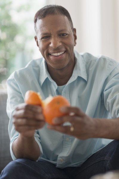 Portrait of smiling man peeling orange fruit.