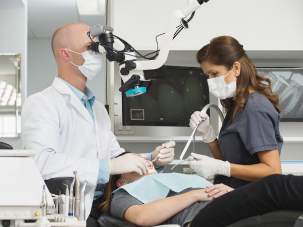 Dentist operation on patient and using microscope.