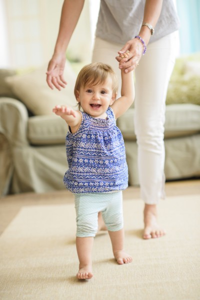 Mother assisting baby daughter (18-23 months) with her first steps.