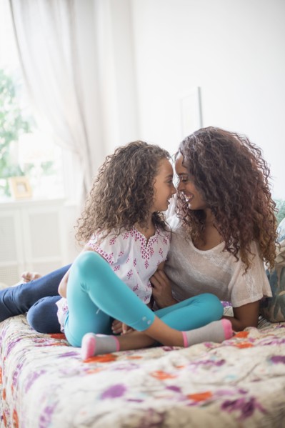 Mother and daughter (8-9) rubbing noses on bed.