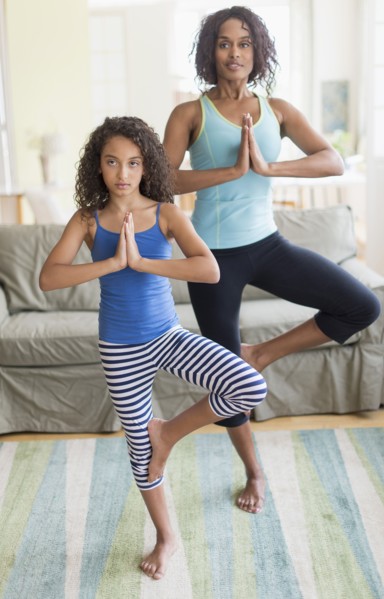 Mother and daughter (8-9) doing in yoga poses in living room.