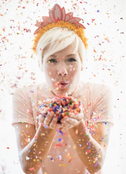 Woman wearing tiara blowing confetti.