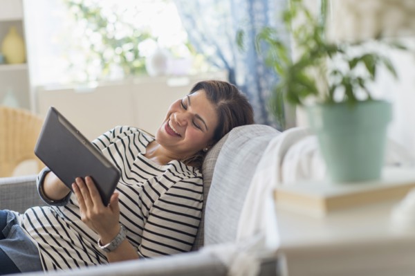 Portrait of happy woman lying on sofa with tablet pc.