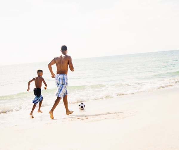 Father and son (10-11) playing soccer on beach