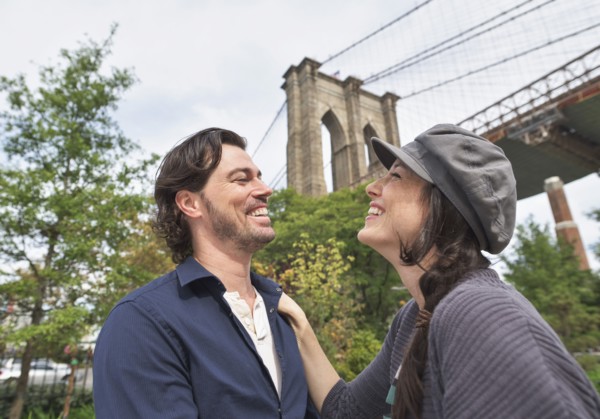 Happy couple standing against Brooklyn Bridge. Brooklyn, New York.