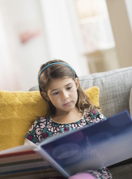 Girl (6-7) reading book at home.