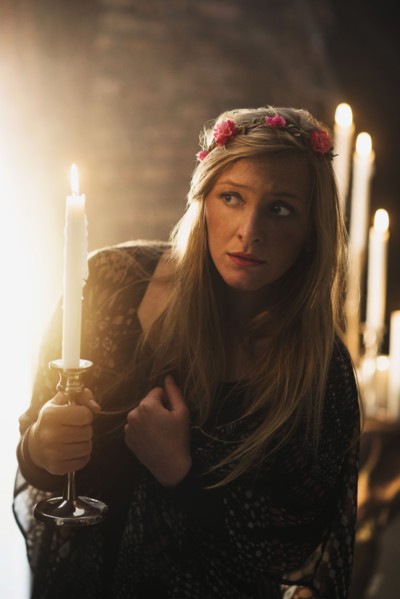 Sorceress holding candle in dark room.