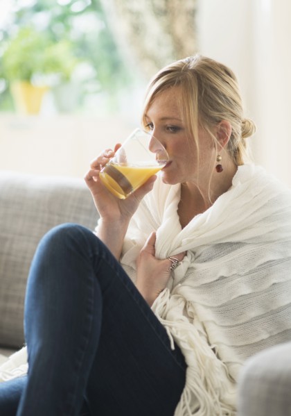 Woman sitting on sofa and drinking orange juice.