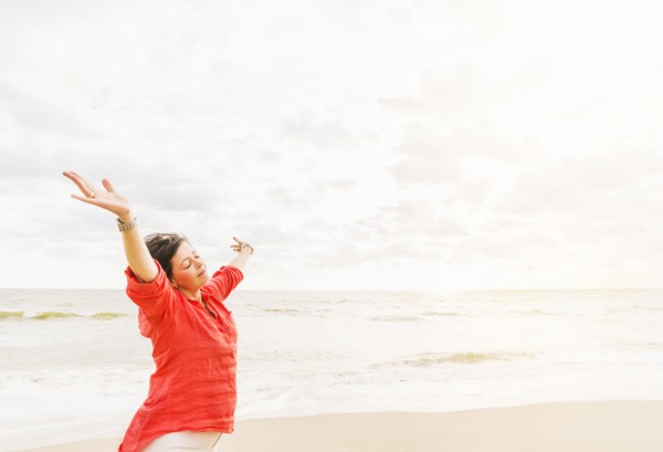 Side view of woman standing with arms up on beach