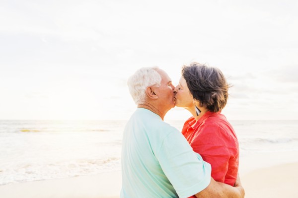 Older couple kissing on beach at sunrise