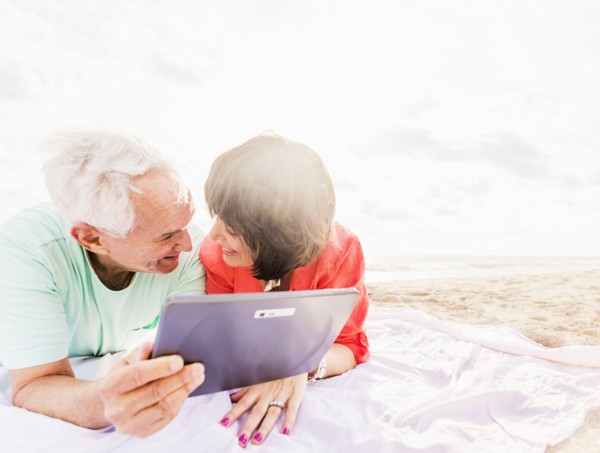 Couple with digital tablet lying on blanket at beach