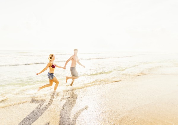 Young couple running in surf holding hands