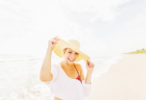 Portrait of smiling young woman on beach wearing sun hat