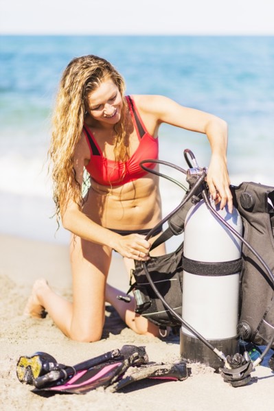 Young woman kneeling on sandy beach putting together scuba diving equipment