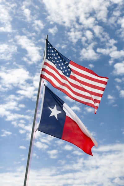 American and Texas flags against cloudy sky