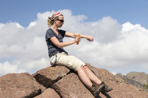 Woman sitting on rock and applying suntan lotion
