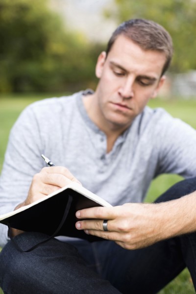 Portrait of young man writing journal in park