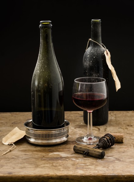 Still life with red wine glass and bottles on wooden table, studio shot.
