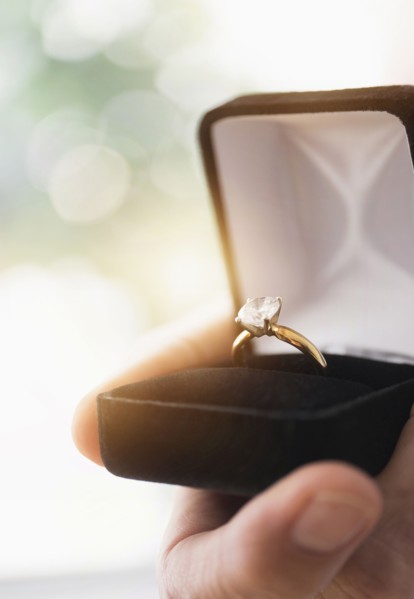 Close up of man's hand holding open box with engagement ring.