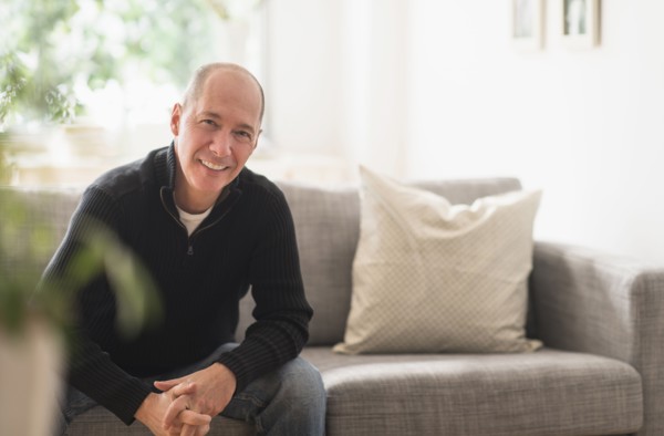 Portrait of smiling mature man relaxing on sofa in living room .