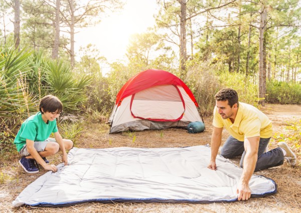 Father and son (12-13) preparing sleeping bag for camping