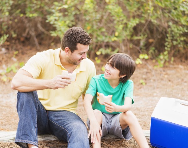 Father and son (12-13) eating sandwiches in forest