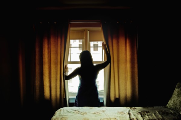 Rear view of female opening curtains at bedroom window