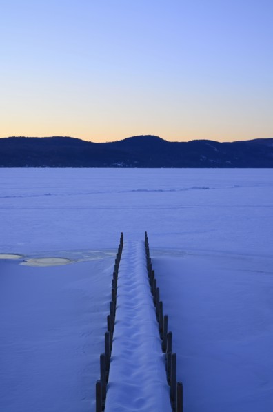 Symmetrical image of snowed jetty with footprints at dawn, hills on horizon