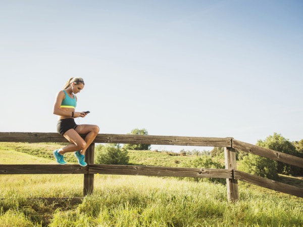 Woman sitting on fence, using smart phone