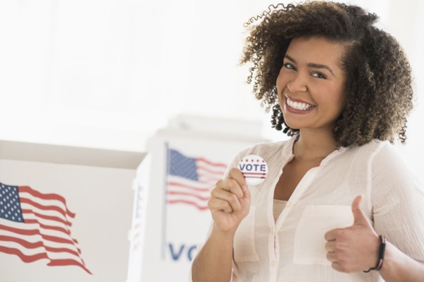 Young woman holding voting badge and smiling.