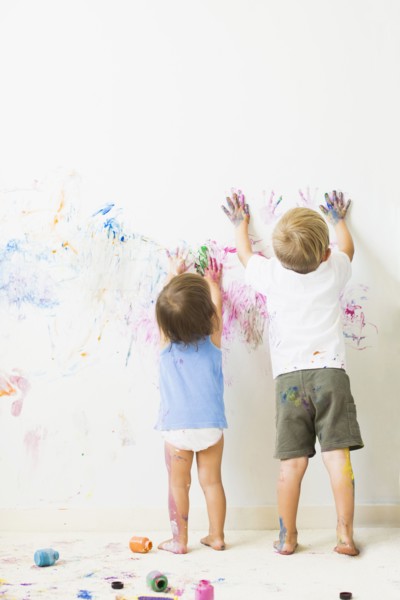 Children (2-3) painting on wall, rear view