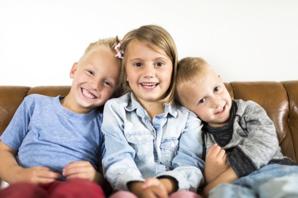 Smiling children (2-3, 4-5) sitting on sofa