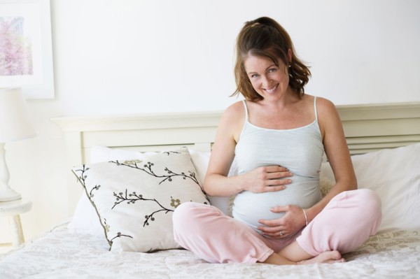 Smiling pregnant woman sitting on bed.