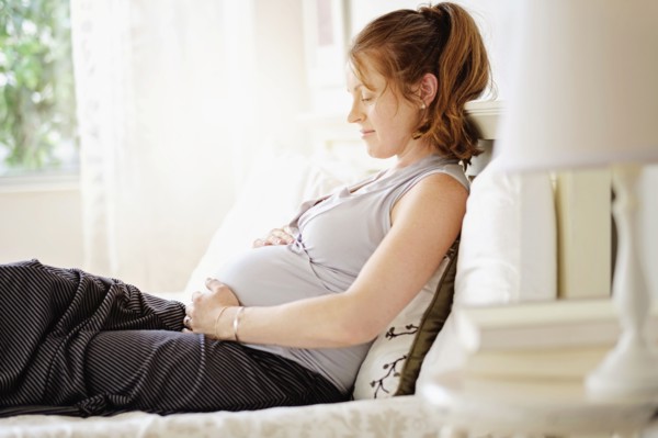 Smiling pregnant woman sitting on bed.