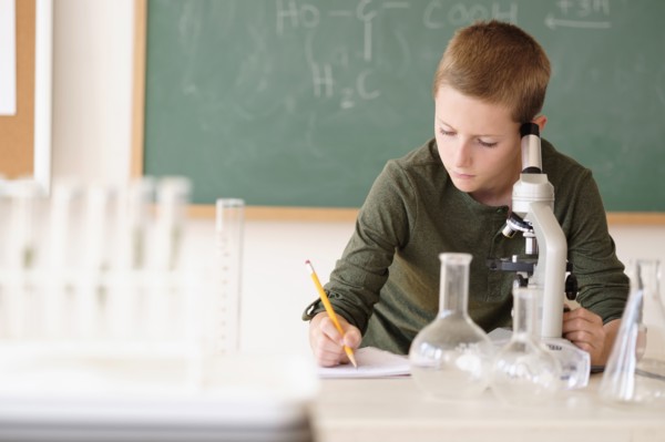 Boy (8-9) taking notes in classroom.